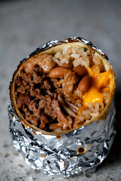 Delicious grilled chicken and vegetable burrito cut open on rustic table with melted cheese and fresh ingredients for Burrito Day celebration