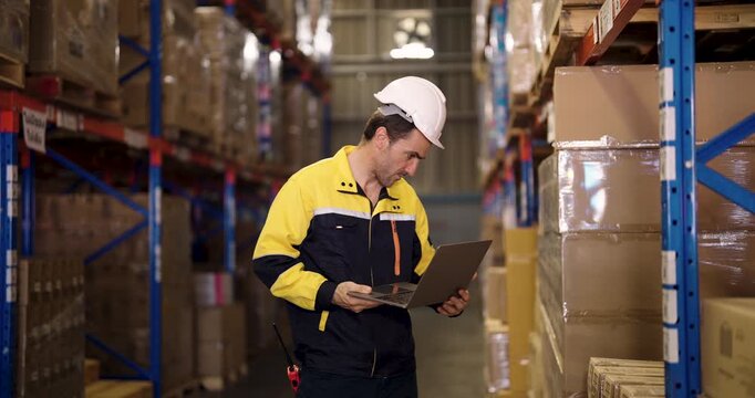 Caucasian male logistic staff using laptop to scan barcodes and check inventory on cardboard boxes placed on warehouse racks in industrial stockroom during inspection routine