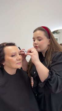 Makeup artist applying false eyelashes eyelash extensions to mature senior elderly woman client anti-aging eye enhancement for older generation retirement age empowerment