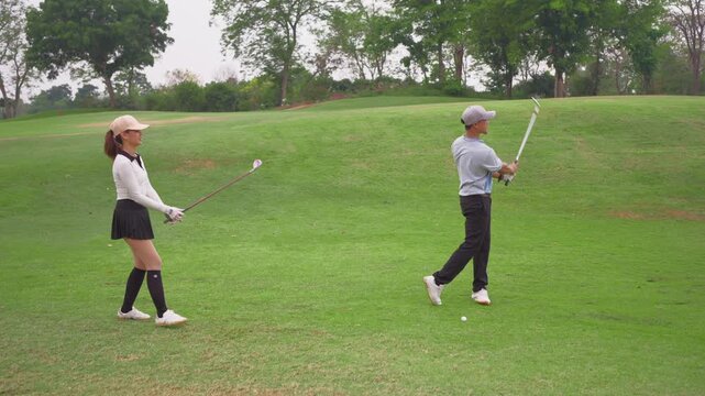 Asian young couple golfer swing clubs together on a scenic golf course. 