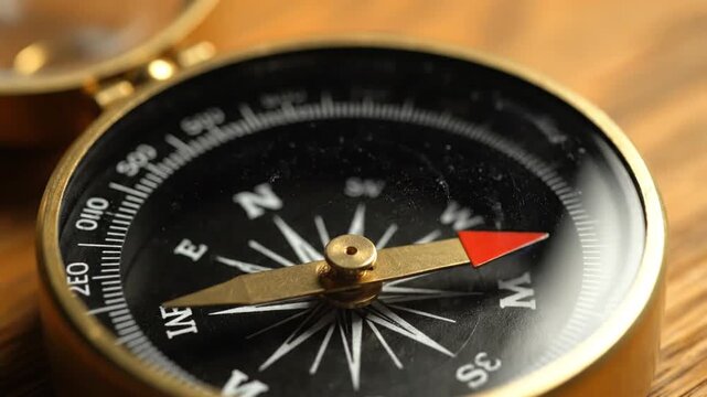 Close-up of a vintage brass compass with a spinning needle on a wooden surface