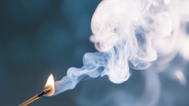 A close up view of swirling smoke rising from a burning matchstick against a soft blue background. The delicate patterns of smoke create an ethereal and mysterious atmosphere