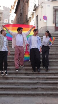 Happy group of young diverse friends walking down city stairs with a rainbow flag. Lgbtqia plus community celebrating pride day together