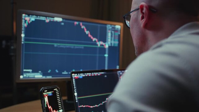 Man in trader home office. Monitor and laptop are on table. Trading program or exchange. Male analyzes candlestick charts for crypto market. Managing Investment portfolio, monitoring financial data