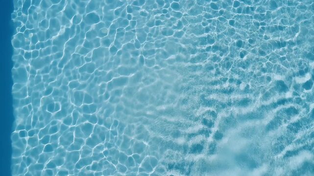 Top down view of clear blue swimming pool water with sunlight caustics and gentle ripples creating an abstract background texture