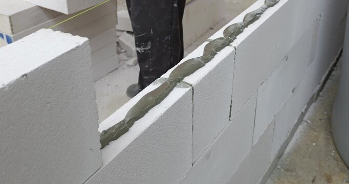 Watch skilled workers laying blocks to create a sturdy wall showcasing bricklaying techniques in a bustling construction site.