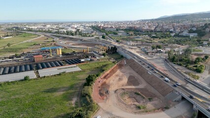 Highway interchange construction site with active traffic and ongoing civil engineering works, expanding urban infrastructure and linking industrial areas with residential zones
