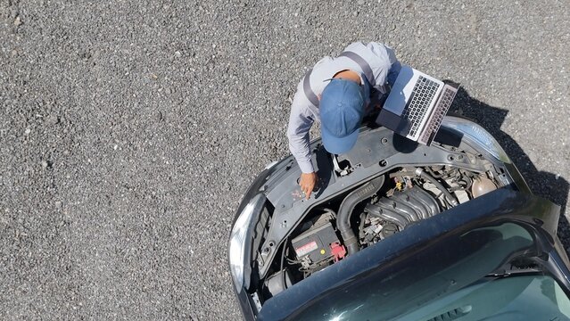Mechanic working on a vehicle, performing diagnostics and maintenance with a laptop open on the car hood, analyzing engine systems for repair and service