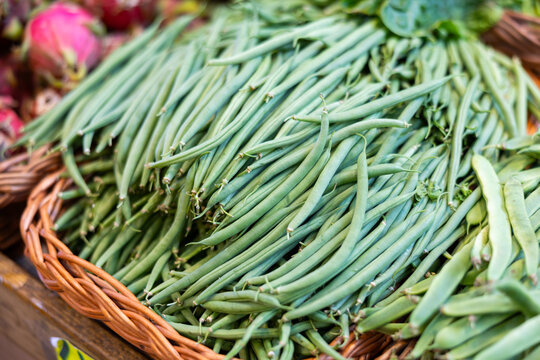 Bunch of fresh green beans lie on counter in vegetable market close-up