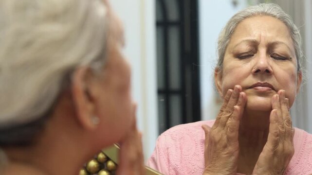 Senior indian woman touching face check facial wrinkles looking in mirror reflection, Old mature 60s female concern about her face skin. Aging process. 4k