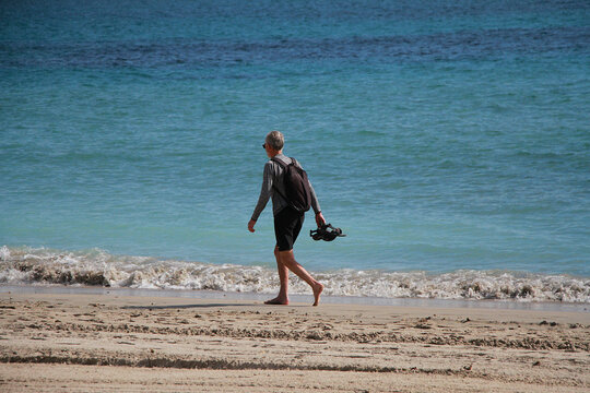 Paseo por la orilla del mar descalzo en vacaciones de verano con chanclas en la mano bajo el sol