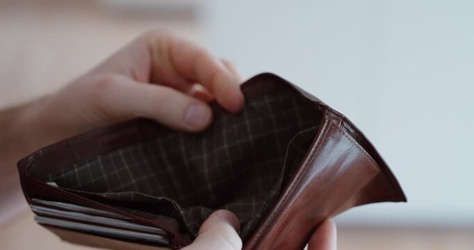 Close-up of a man opening an empty wallet with no money inside. Concept of financial stress, debt, poverty, economic crisis and personal money problems.
