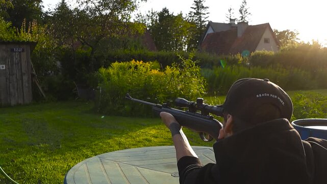 Focused shooter aiming at small backyard target with sunlight rays and visible recoil