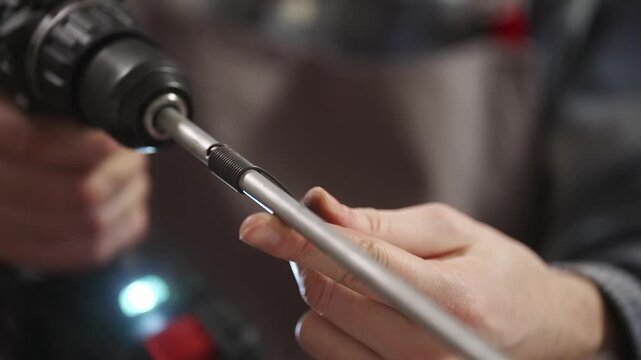 Macro close up of hands using cordless drill to thread metal rod. Mechanical workshop process, engineering detail, DIY metalworking and industrial production concept.