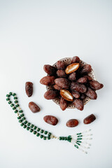 Fototapeta premium Minimalistic flat lay with a bowl of dates and green prayer beads chain