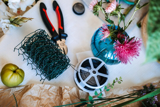 High angle view of florist tools and materials including wire mesh and flowers on table. Eco-friendly floristry, sustainable floral design, chicken wire technique, plastic-free mechanics.