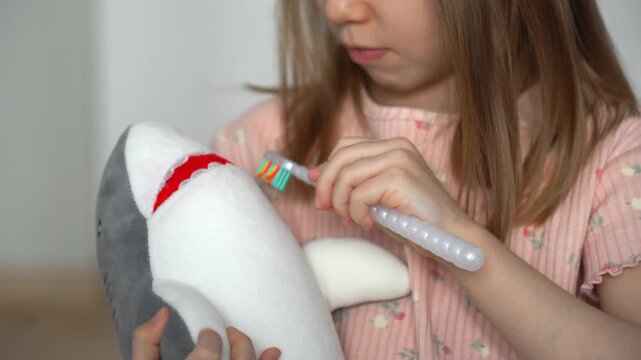 Close up of little girl brushes teeth of toy shark. Childrens hands with toothbrush. Oral hygiene. Health care