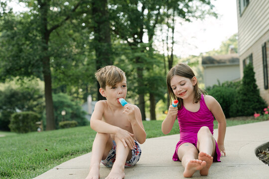 Two kids eating red white blue popsicles outside