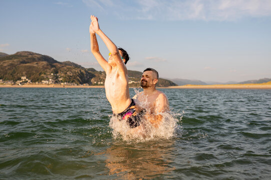 Father playfully throwing teenage son into sea water.