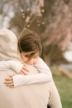 Child hugging parent under blooming cherry tree