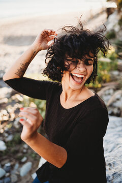 Beautiful hispanic woman with wavy hair laughing dancing at beach