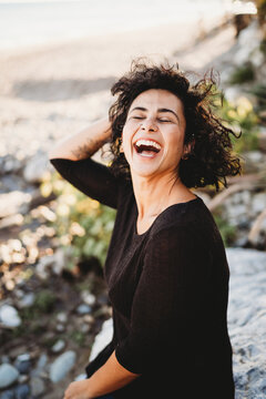 Beautiful hispanic woman with wavy hair laughing dancing at beach