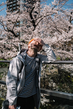 Man in gray coat with camera squinting in cherry blossoms spring