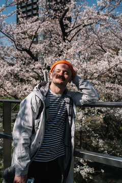 Man in gray coat with camera squinting in cherry blossoms spring