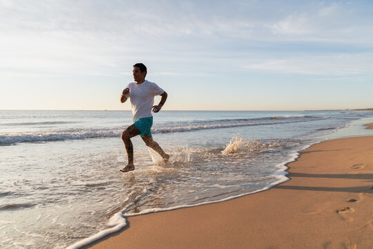Man jogging barefoot along beach splashing ocean water
