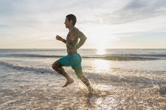Male athlete running in ocean surf at sunset