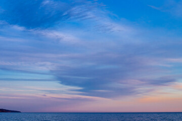 Obraz premium a calm ocean horizon under a vibrant twilight sky, featuring a soft gradient of warm orange near the waterline that gently fades into deep blue with wispy, streaky clouds.