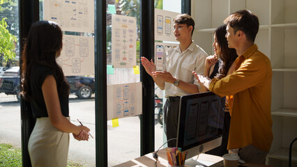 UX UI design team collaborating around a desk with mobile app wireframes and interface layouts, discussing user experience, usability, and digital product design. © matinee