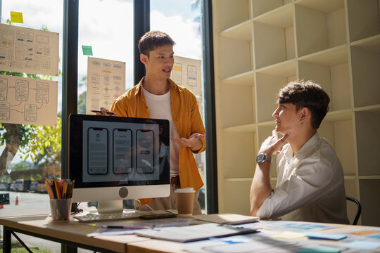 UX UI design team discussing mobile app wireframes on a desktop screen during a collaborative meeting