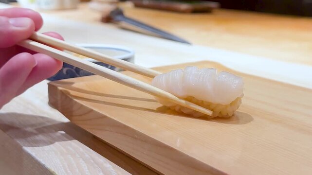 Close Up of Chopsticks Picking Up Scallop Nigiri Sushi from Wooden Board