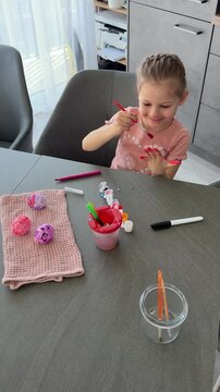 Child smiling while painting Easter eggs at the table. Joyful participation in seasonal family traditions.