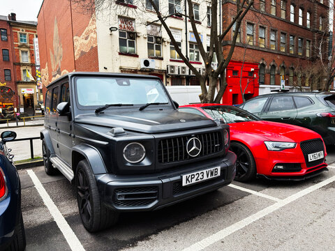 Luxurious black Mercedes G 63 Class and red sports car parked on Manchester street