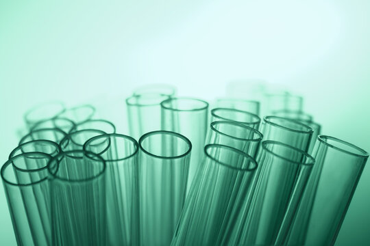 Transparent laboratory test tubes form abstract medical background with soft green gradient light and wide copy space for research.