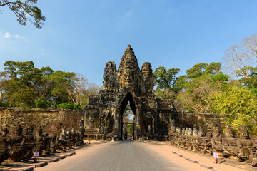 Fototapeta premium Wide frontal view of the iconic south gate of Angkor Thom near Siem Reap, Cambodia, featuring towering carved stone architecture flanked by rows of guardian statues. The ancient Khmer gateway stands