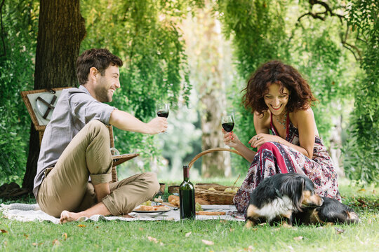 Couple with dog having a picnic in a park drinking red wine
