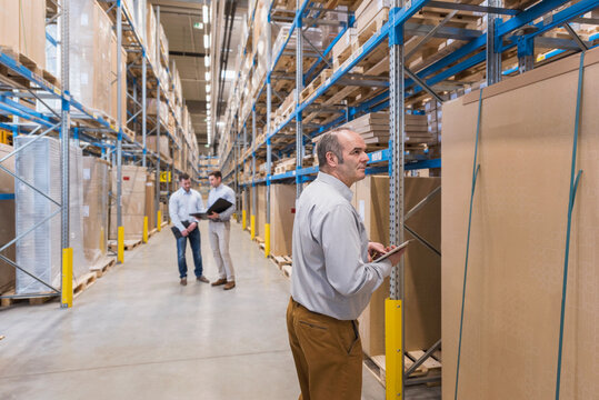 Man with tablet and two men with folder in factory warehouse