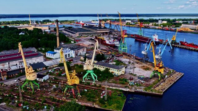 Top down perspective of a large shipyard with cranes and dry docks on the banks of a large river.