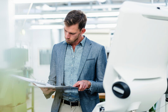 Male professional looking at plan in file document at factory
