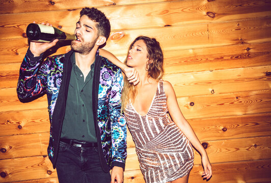 Young woman leaning on male friend drinking champagne against wall in party