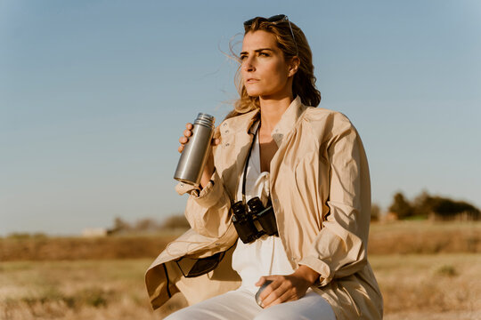 Female traveller with binoculars drinking thermos flask
