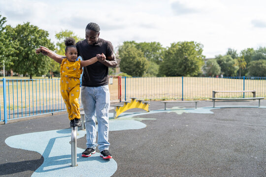 Father helping daughter balancing on a bar on a playground