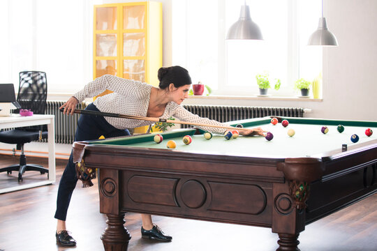 Determined businesswoman playing pool billard in modern office