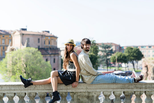 Happy young couple sitting back to back on balustrade