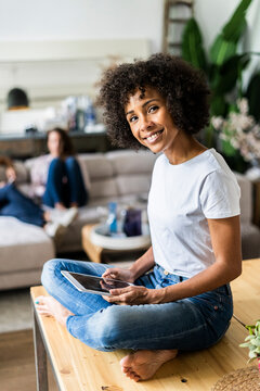 Portrait of smiling woman with tablet on table at home with friends in background