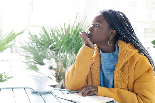 Pensive young woman with note book at pavement cafe looking at distance