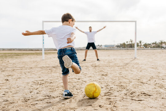 Man and boy playing soccer on the beach